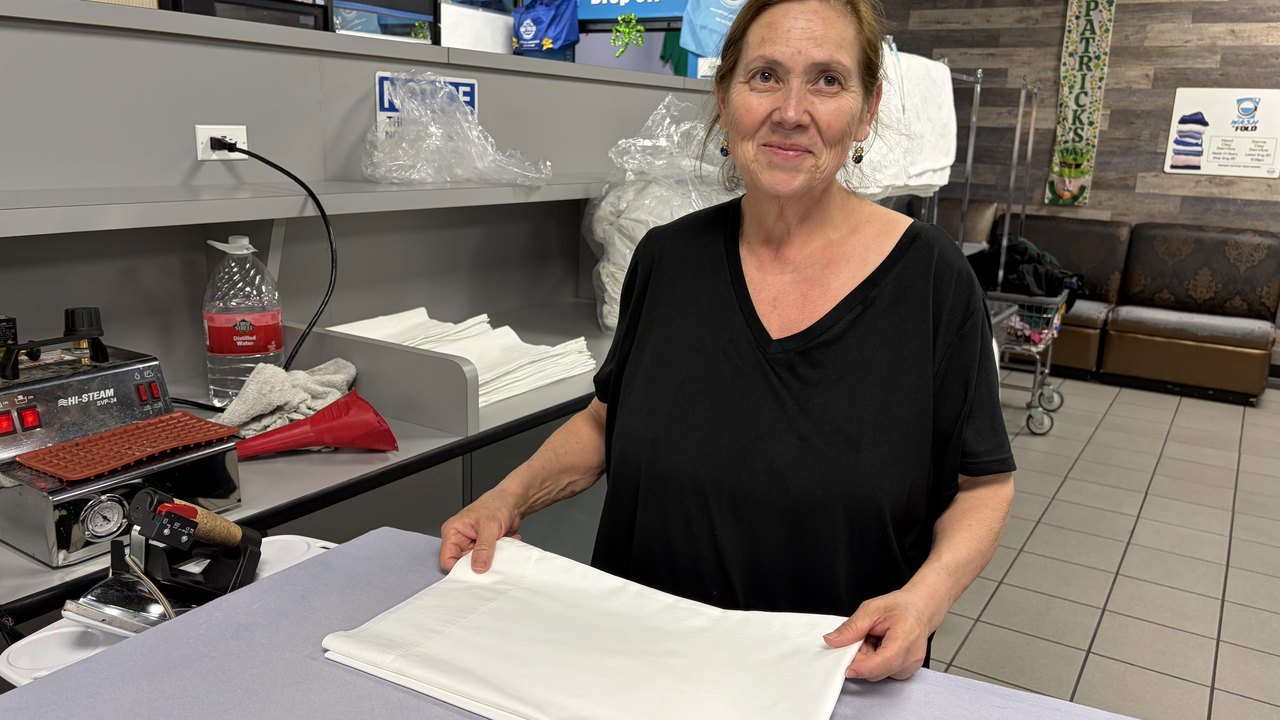 Half Price Laundry team member folding a pressed white table linen at the wash and fold counter